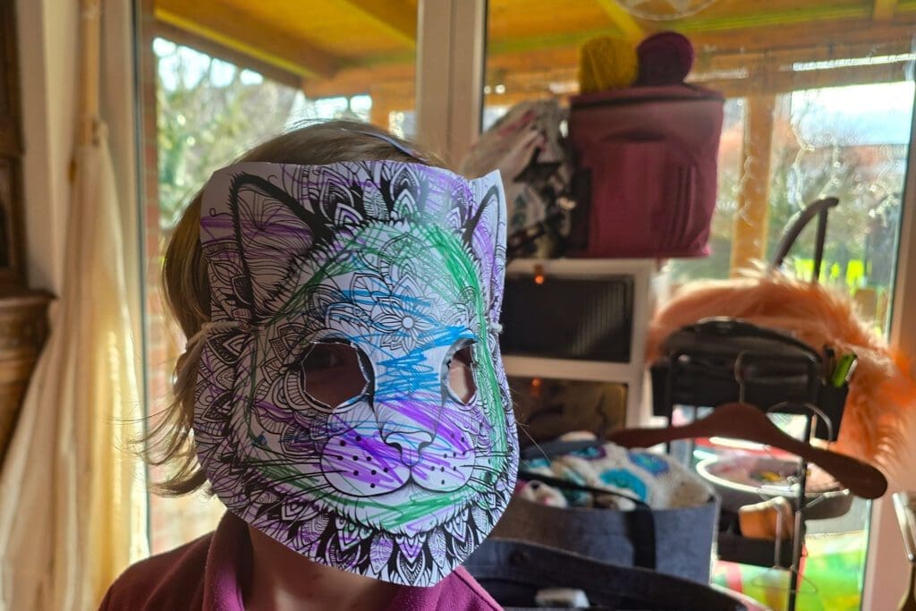 Kind vor einem Fenster, dass eine Papiermaske in Katzenform trägt.