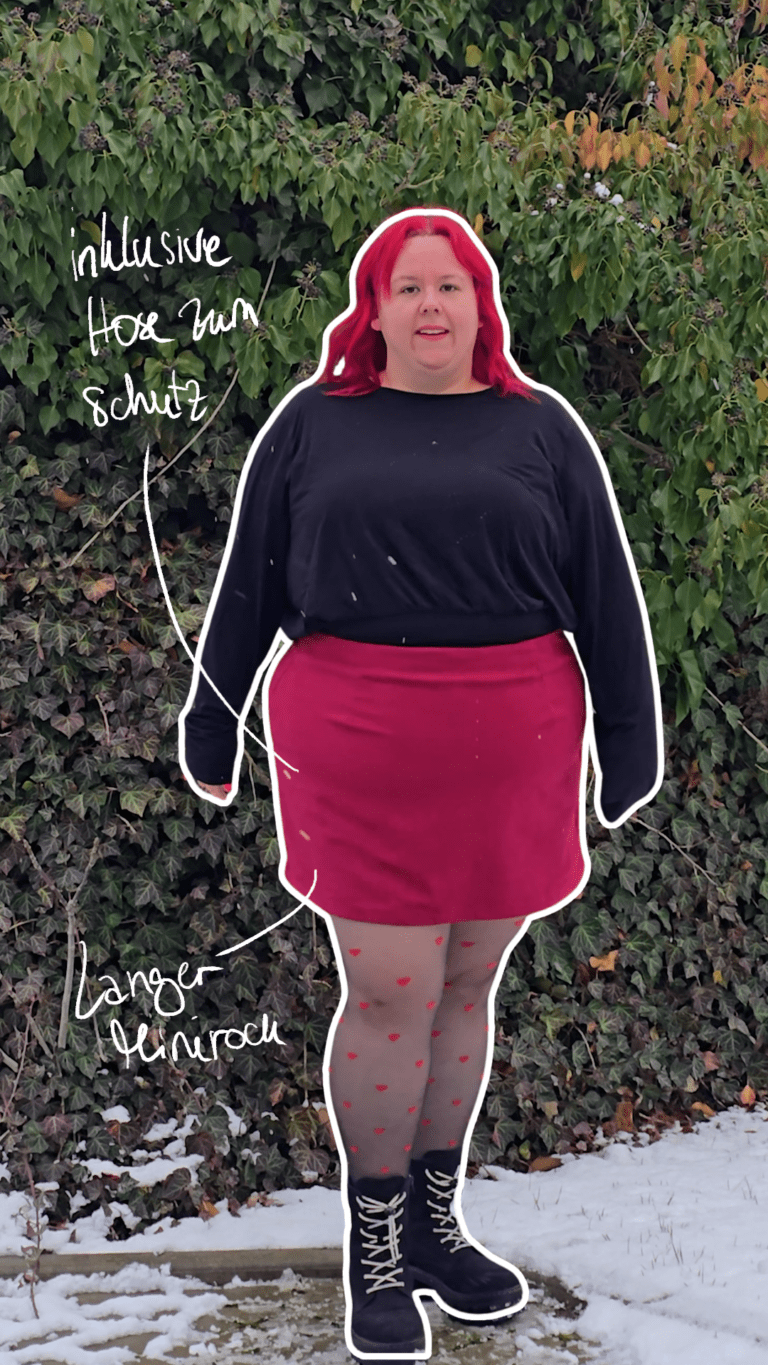 Dicke rothaarige Frau trägt schwarze Stiefel, eine Strumpfhose mit Herzen darauf, einen kurzen roten Cord-Rock und einen schwarzen Pullover.