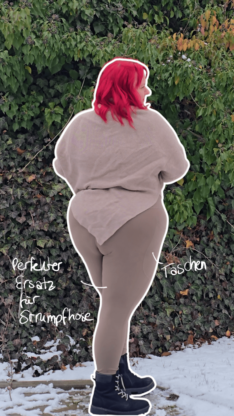 Dicke rothaarige Frau trägt schwarze Stiefel, eine beige Hose und einen beigen Poncho-Pullover. Sie steht mit dem Rücken zur Kamera.