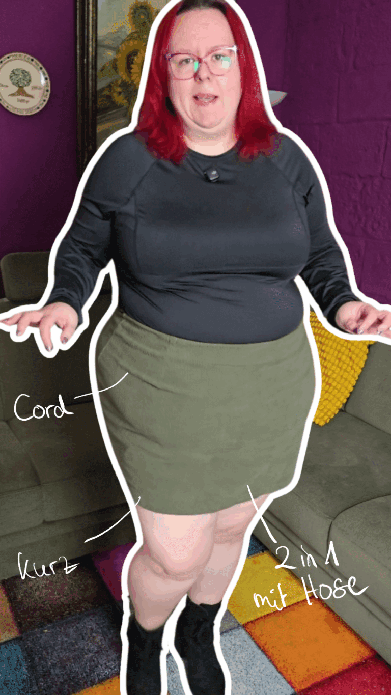 Dicke rothaarige Frau trägt ein schwarzes langärmeliges Oberteil und dazu einen Cordrock in graugrün und schwarze Stiefeletten.